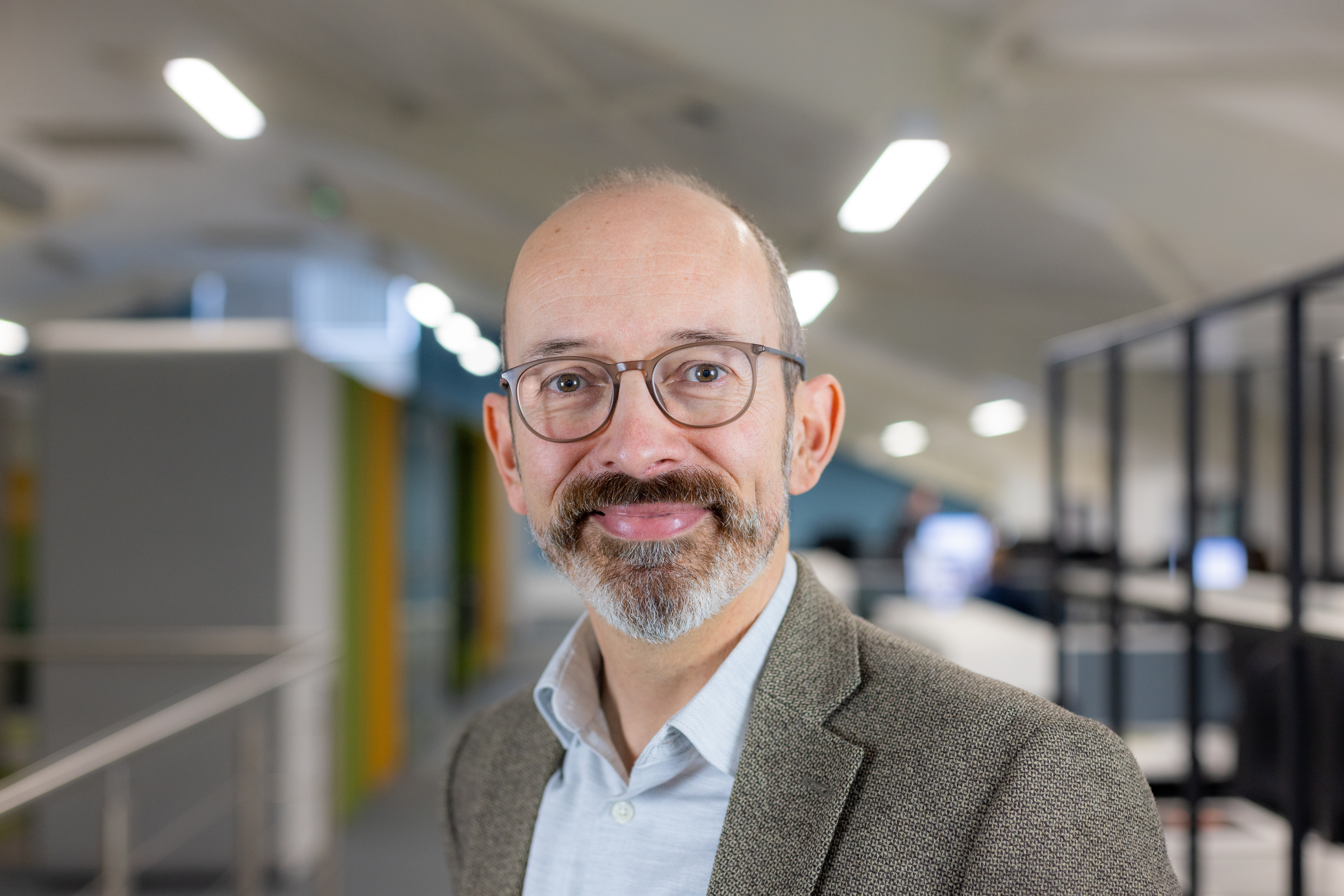 Headshot of Alex Reeve, a smiling man with glasses in a blue shirt and grey blazer