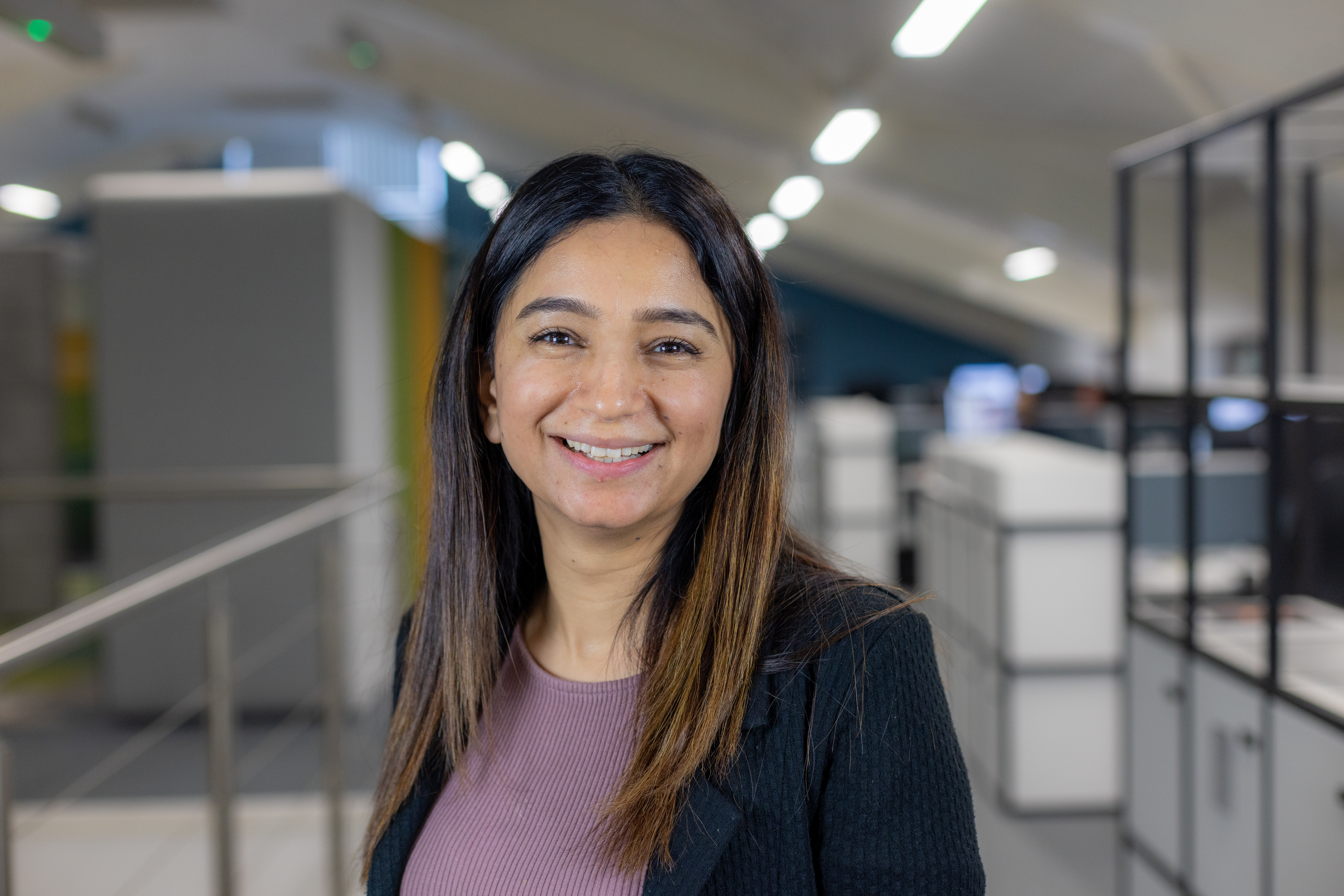Headshot of Ambreen Jahangir, a smiling brunette woman in a purple top and black blazer.