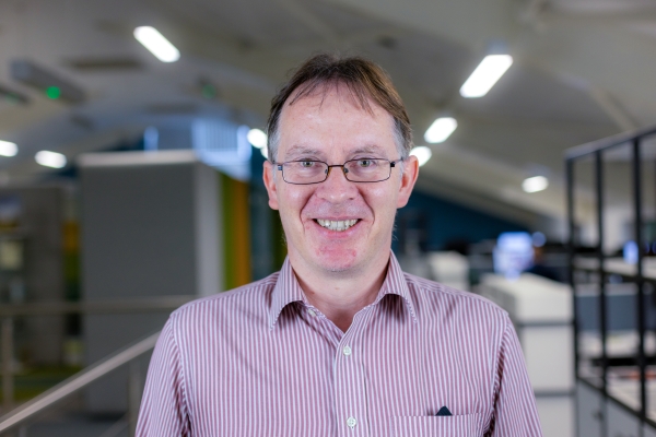 Headshot of Bruce Webb, a smiling man with glasses in a pink and white shirt.
