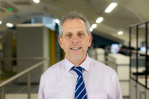 Headshot of Mike Davies, a smiling man in a pink shirt with a navy and pink tie.