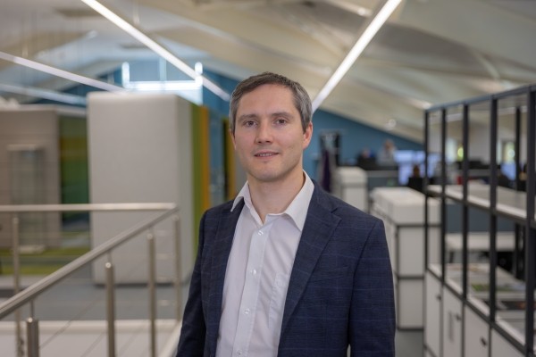 Headshot of Oly Longland, a smiling man in a white shirt and navy blazer.