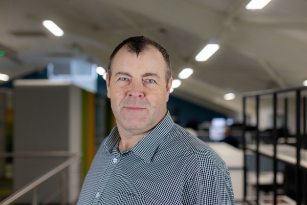 Headshot of Stewart Bethell, a smiling man in a black and white shirt.