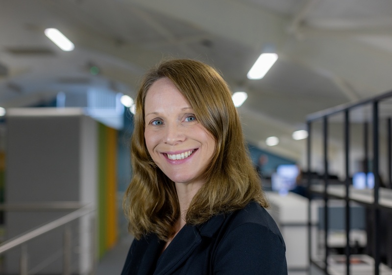 Headshot of Amanda Nolan, a smiling woman with dark ginger hair in a black top and blazer