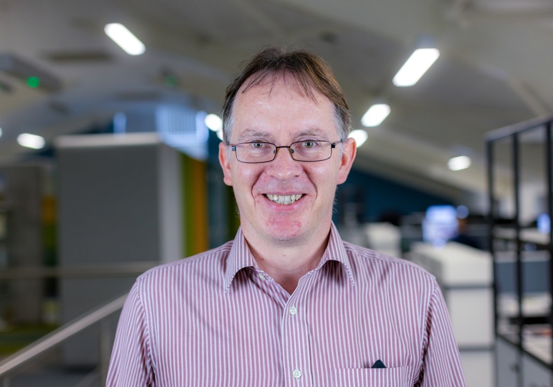 Headshot of Bruce Webb, a smiling man with glasses in a red and white shirt 