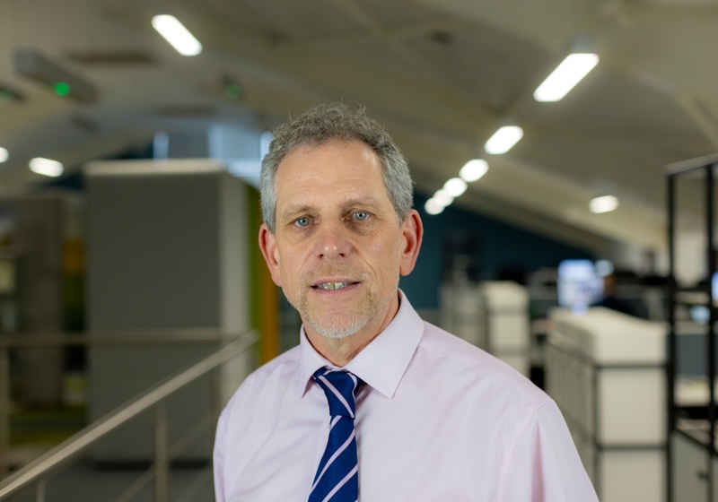 Headshot of Mike Davies, a smiling man in a pink shirt and blue tie