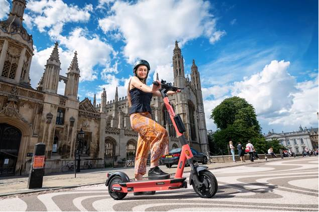 Image of a young female riding a Voi Scooter outside Kings College, Cambridge.